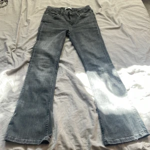 Grå bootcut jeans från Gina Tricot - Snygga grå jeans från Gina Tricot med bootcut passform. Klassisk femficksmodell och normal midja. Jeansen är i mjukt denimtyg och har en lätt utsvängd siluett som ger en cool vibe.Jeansen har även ett håll på vänstra benet backbenet.