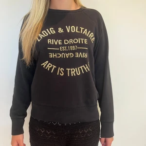 Svart sweatshirt Zadig & Voltaire guldtext - Cool svart sweatshirt från Zadig & Voltaire med broderad guldig text framtill. Tröjan har rund hals och långa ärmar. Som man kan se på bild har några trådar på den broderade guldtexten lossnat. Hör av er vid fler frågor eller funderingar!