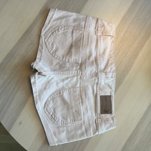 Ljusrosa jeansshorts Tally Weijl - Snygga ljusrosa jeansshorts från Tally Weijl med råa kanter och slitna detaljer. Shortsen har två knappar framtill, klassiska fickor och en läderpatch med logga bak. Perfekta för varma dagar när du vill ha en chill och trendig look. Populära så var snabba!!