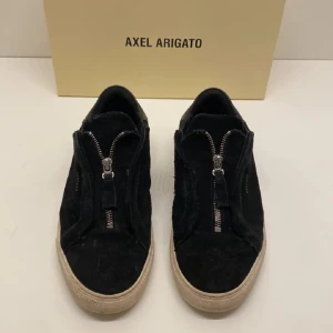 Svarta sneakers från Axel Arigato - Snygga svarta sneakers från Axel Arigato med dragkedja framtill.                                                 Ordinarie pris=2200