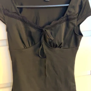 Svart topp med spetsdetaljer - Snygg svart topp med spetsdetaljer och knytning framtill. Toppen har korta ärmar och en åtsittande passform som framhäver figuren. Perfekt för en stilren look.