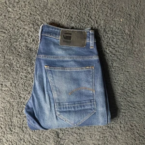 G-star Jeans - Snygga blå jeans från G-Star RAW med en klassisk femficksdesign och subtila slitningar för en trendig look. Jeansen har en rak passform och är tillverkade i ett slitstarkt denimtyg. Perfekta för en avslappnad stil.
