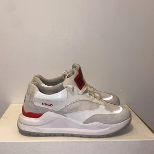 Beige sneakers från Hugo - Snygga beige sneakers från Hugo med röda detaljer och logotyp. Skorna har snörning och en bekväm sula. Perfekta för en stilren look.