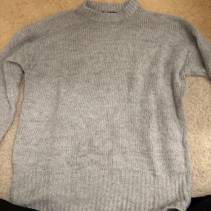 Grå stickad tröja från lager 157 - Mysig grå stickad tröja från 157 med hög krage. Perfekt för kyliga dagar med sin mjuka och bekväma passform. Tröjan har långa ärmar och ribbade kanter som ger en stilren look.