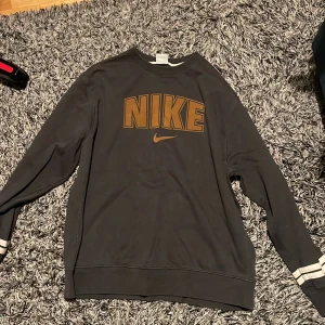 Svart långärmad tröja från Nike - Säljer en svart långärmad tröja från Nike med stort retro märke i mitten färgat guld typ. (Retro stämplad tröja) . Pris går att diskuteras. 