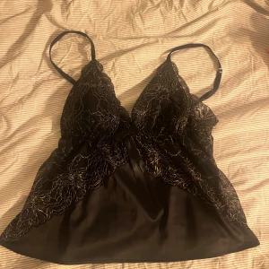 Svart spetslinne med justerbara axelband - Elegant svart linne med spetsdetaljer och justerbara axelband. Perfekt för en stilfull look med en touch av glamour.