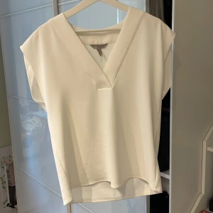 Vit blus från H&M - Säljer en stilren vit blus från H&M i storlek 36. Blusen har en v-ringad design och korta ärmar, perfekt för en elegant look. Materialet är mjukt och bekvämt, vilket gör den idealisk för både vardag och mer formella tillfällen. Nytt skick men utan lapp. 