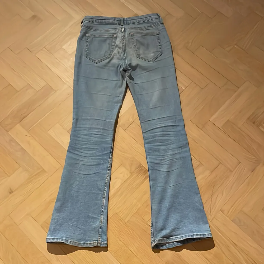 Säljer ett par blå flared jeans från H&M med justerbar och låg midja. De har en klassisk femficksdesign och är perfekta för en avslappnad stil. Storlek 152, innerbenslängd är 70cm. Har en igenstydd reva på ena byxbenet vilket syns på bild. Farkut & Housut.