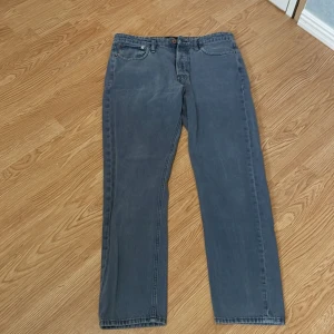 Grå jeans från Jack & Jones Storlek 32/32 - Snygga grå jeans från Jack & Jones med en klassisk straight fit. De har en knappgylf och femficksdesign. Perfekta för en avslappnad stil. Längden är 32 samt bredden är 32