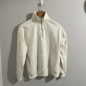 Vit tröja med dragkedja - Säljer en stilren vit tröja med hög krage och dragkedja. Perfekt för en avslappnad look. Tröjan har långa ärmar och är gjord i ett mjukt material som känns skönt mot huden.