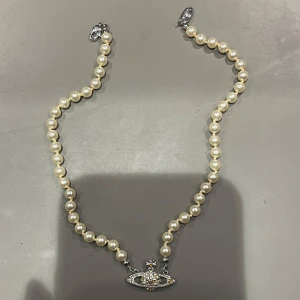 Vivienne Westwood halsband - Vivienne Westwood-halsband, pärlorna är i bra skick men flera stenar i smycket har missfärgats eller fallit av. Därför är priset lågt.