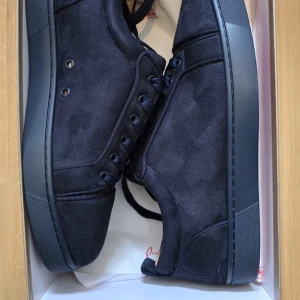 Mörkblå sneakers från Christian Louboutin - Snygga mörkblå sneakers i mocka från Christian Louboutin med den ikoniska röda sulan. Skorna har snörning och en stilren design som passar perfekt för en trendig look. Ej använda samt helt nya. Pris kan diskuteras vid snabb affär!