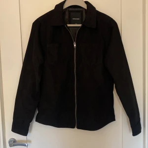 Svart jacka från Jack & Jones - Snygg svart jacka från Jack & Jones med dragkedja framtill. Jackan har en klassisk krage och långa ärmar, perfekt för en stilren look. Passar bra till både vardag och mer uppklädda tillfällen.