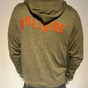  hoodie från Zadig Volatair - Snygg grön hoodie med dragkedja och huva. På baksidan finns ett orangea Voltaire tryck. Perfekt för en avslappnad stil. Den har långa ärmar och ribbade muddar.
