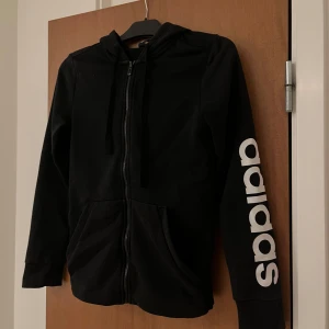 Svart hoodie från Adidas - Säljer en svart hoodie från Adidas med dragkedja och luva. Adidas-loggan är tryckt i vitt på ena ärmen. Köpt för 669 på Zalando. Pris går att diskutera