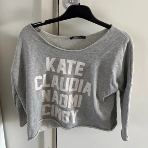 Grå croppad tröja med namntryck - Snygg grå croppad tröja från Gina tricot med tryck av namn i vitt. Tröjan har en avslappnad passform och långa ärmar, perfekt för en casual look. Den är mjuk och bekväm att bära. Storlek XS