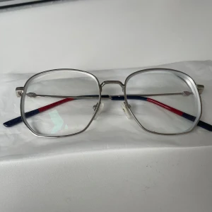 Gucci Silvriga glasögon med färgglada skalmar - Snygga glasögon med en stilren silverfärgad metallram och unika skalmar i blått och rött. Den geometriska formen ger en modern touch. Perfekta för dig som vill ha något annorlunda och trendigt.