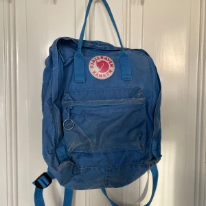 Blå ryggsäck från Fjällräven Kånken - Säljer en klassisk blå Fjällräven Kånken ryggsäck. Den har ett stort huvudfack, en dragkedjeficka framtill och två sidofickor. Ikonisk logga på framsidan. Perfekt för vardagsbruk eller utflykter.