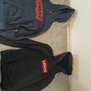 Mörkblå hoodies från Levi's - Två mörkblå hoodies från Levi's med det klassiska röda logotyptrycket på bröstet. Båda tröjorna har en stor ficka framtill och justerbar huva med dragsko. Perfekta för en avslappnad stil.
