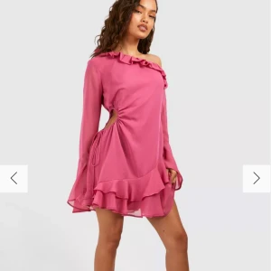 Rosa offshoulder klänning med volang - Helt oanvänd och ny med prislappen kvar. Snygg rosa offshoulder klänning med volangdetaljer och lång ärm. Klänningen har en unik design med snörning i sidan och en luftig, fladdrig kjol. Perfekt för en trendig look! 