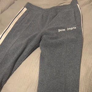 Grå mjukisbyxor från Palm Angels - Snygga grå mjukisbyxor från Palm Angels med vit logga på sidan. Byxorna har en elastisk midja och vita ränder längs sidorna. Köpa för 4000 men säljer för 2000