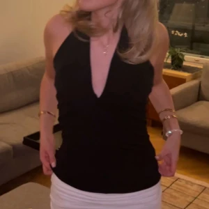 Svart halterneck topp med v-ringning - Snygg svart halterneck topp med djup v-ringning framtill. Toppen är ärmlös och har en tight passform som framhäver figuren. Perfekt för dig som vill ha en stilren och trendig look.