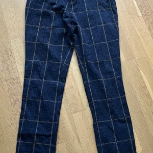 Mörkblå rutiga byxor från Para Mi - Snygga mörkblå byxor från Para Mi med rutigt mönster i beige. Modellen är high waist och extra skinny leg. Materialet är en mix av bomull, polyester och elastan som ger stretch och bekväm passform. Perfekta för dig som gillar stilrena men ändå unika byxor.