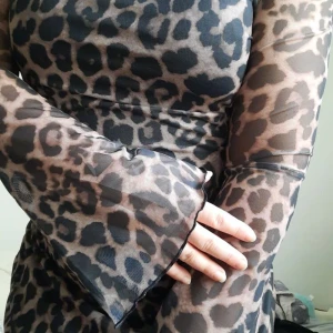 Leopardmönstrad meshklänning - Snygg kort klänning i mesh med leopardmönster. Klänningen har långärmade, lätt utsvängda ärmar och figurnära passform. Färgerna går i svart och beige, vilket ger en cool och trendig look.