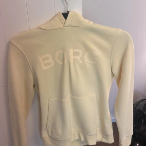 Ljusgul hoodie från Björn Borg XS - Säljer en ljusgul hoodie från Björn Borg i storlek XS. Tröjan har en stor huva, magficka och tryckt BORG-logga framtill. Mjuk och skön bomullsmix, perfekt för chill dagar. Långärmad och med klassisk passform.