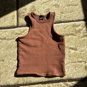 Brun ribbad linnetopp Gina Tricot - Säljer en brun ribbad linnetopp från Gina Tricot i storlek XS. Toppen har klassisk rak passform, ärmlös design och rund halsringning. Perfekt att styla med jeans eller kjol för en chill look.