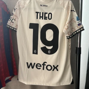 AC Milan Theo Hernandez 19 fotbollströja Puma  - AC Milan 2023/2024 Serie A matchtröja med Theo och nummer 19 på ryggen. Tröjan är ljusbeige med unikt mönster i champagne och svarta detaljer, tillverkad i lätt och ventilerande polyester. Svart V-ringad krage, korta ärmar och tryck från Puma och Emirates.