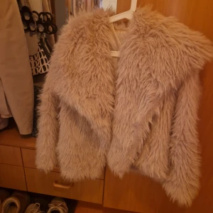 Beige fluffig pälsjacka - Supermjuk och fluffig beige pälsjacka med bred krage och långa ärmar. Jackan har en oversized känsla och stängs med en diskret metallknapp. Perfekt för dig som vill sticka ut och hålla dig varm under kyliga dagar. Jackan är storlek M men passar S också! Fukspäls
