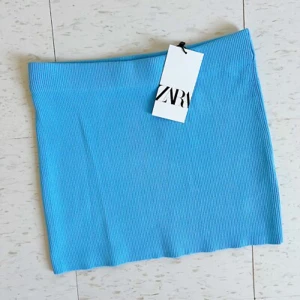 Blå ribbad kortkjol från Zara - Snygg blå ribbad minikjol från Zara med rak passform. Kjolen har en enkel design utan detaljer och är gjord i ett stretchigt syntetmaterial som sitter bekvämt. Perfekt för dig som gillar färg och vill ha en fräsch look.