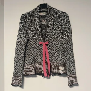 Mönstrad cardigan jacka Odd Molly - Supersnygg svartvit cardigan jacka från Odd Molly med stickat mönster, lång ärm och rosa knytband framtill. Jackan har en unik mix av grafiska mönster och vågig kant nertill. Perfekt för dig som vill sticka ut med en cool och mysig look. Använd ca 2 gånger, tvättat 1 gång, mest hängt i garderoben💓