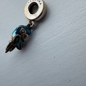 Pandora berlock med blå papegoja - Unik berlock från Pandora i form av en papegoja med detaljer i blått, grönt och gult. Tillverkad i äkta silver med färgglad emalj som ger en cool och tropisk vibe. Perfekt att hänga på ditt armband för att ge det lite extra personlighet. orginalpris 880kr mitt pris 450