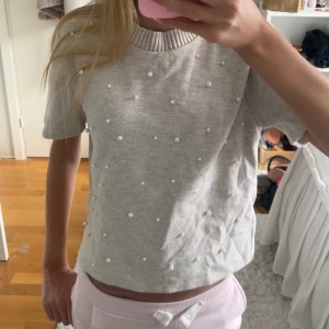 Beige stickad pärltröja från Zara - Superfin beige stickad tröja från Zara med korta ärmar och ribbad hals. Tröjan har pärlor över hela framsidan och är fint skick! 