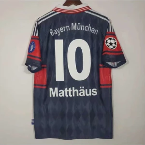 Bayern München Matthäus fotbollströja - Retro Bayern München fotbollströja med nummer 10 och Matthäus på ryggen. Tröjan är mörkblå med subtilt rutmönster, röda och svarta detaljer på ärmarna samt vita tryck. Klassisk krage med röda ränder och Champions League-märke på ärmen.
