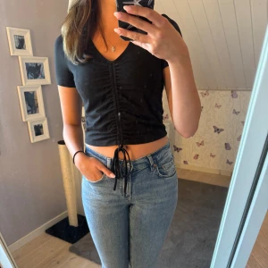 Svart topp med snörning - Svart topp med v-ringning och snörning framtill som ger en rynkad effekt. Storlek M men passar S. Använd fåtal gånger💞