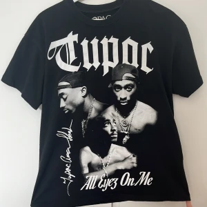 Svart Tupac t-shirt Pull&Bear XS - Svart t-shirt från Pull&Bear med stort Tupac-tryck och texten 'All Eyez On Me' framtill. Rund hals och korta ärmar. Materialet är mjuk bomull och passformen är normal/ oversize. Den är i storlek XS men passar en S eller M person beroende på hur man vill att den ska sitta. Perfekt för dig som gillar streetstyle och hiphop.