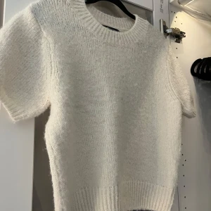 Vit stickad tröja från Gina Tricot - Supermysig vit stickad tröja från Gina Tricot med korta ärmar och rund hals. Tröjan har en fluffig känsla och ribbade detaljer vid hals, ärmslut och nederkant. Använd max 2-3 gånger. Nypris 299