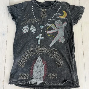 Svart t-shirt Shiroi Neko Streetgang - Svart t-shirt från Shiroi Neko Streetgang med coolt tryck fram och bak. Framsidan har motiv med ängel, tärningar, diamant, ros och texten Las Vegas. Baksidan har gul text, ros, krona och kors. T-shirten har korta ärmar och en vintage tvättad look.