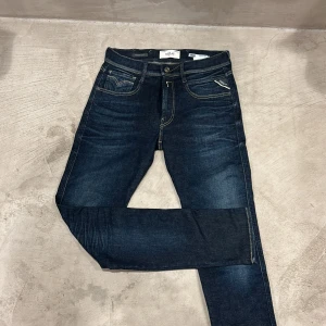 Replay Anbass Hyperflex jeans blå - Snygga mörkblå Replay Anbass Hyperflex jeans med klassisk femficksdesign och kontrastsömmar. Jeansen har normal passform, mellanblå tvätt och är tillverkade i stretchigt jeansmaterial för extra komfort. Perfekta för dig som gillar stilrena och bekväma jeans.