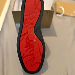 Svarta Christian Louboutin sneakers mocka - Snygga svarta sneakers från Christian Louboutin i mjuk mocka med klassisk röd sula och diskret logga undertill. Skorna har rund tå, svarta snören och en stilren, minimalistisk design som passar perfekt till streetwear eller en mer dressad look. Äkta!!