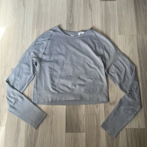 Ljusgrå croppad långärmad tröja - Säljer en ljusgrå/blå croppad långärmad tränings tröja med ribbade muddar och slät framsida. Tröjan har en enkel och clean look, perfekt till träningspasset. Materialet känns mjukt och stretchigt, och passformen är normal med lite kortare längd. Storleken är L men jag skulle nog mer säga att den är en S/M. Den är helt oanvänd, har endast testat den på en gång.