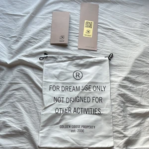 Vit dustbag från Golden Goose - Vit dustbag från Golden Goose med svart tryck och snörning upptill. Perfekt för att förvara dina sneakers eller accessoarer. Snygg och stilren design med texten 'FOR DREAM USE ONLY' på framsidan. Kommer med original tags.