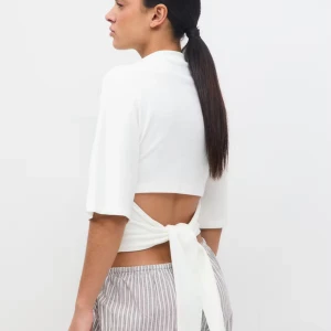 Vit croppad topp med knyt i ryggen - Säljer en vit croppad topp med halvlånga ärmar och hög hals. Toppen har öppen rygg med breda knytband som ger en snygg detalj. Mjuk och stretchig känsla, perfekt för dig som gillar stilrena och trendiga plagg. Tröjan är köpt den här tröjan och är knappast använd. 