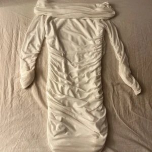 Vit klänning  Gina Tricot M - Säljer en vit klänning från Gina Tricot i storlek M. Klänningen har offshoulder-design, långa ärmar och snygga rynkade detaljer längs hela kroppen. Materialet är mjukt och stretchigt, perfekt för student eller sommarens alla tillfällen.