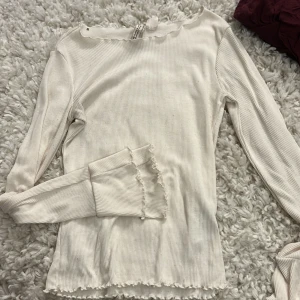 Vit ribbad långärmad topp från H&M  - Säljer en vit ribbad långärmad topp från H&M Divided i storlek XS. Toppen har volangkant vid halsringning, ärmslut och nederkant för en extra söt touch. Perfekt att styla med jeans eller kjol för en chill och trendig look. Ganska genomskinlig 