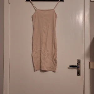 Beige ribbad kort klänning med smala band - Säljer en beige ribbad klänning med smala axelband och rak halsringning. Klänningen är kort och har en slim passform som sitter snyggt mot kroppen. Perfekt för dig som gillar minimalistisk stil och neutrala färger.