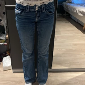 Blå bootcut jeans med låg midja - Säljer ett par klassiska blå jeans med bootcut och låg midja. Jeansen har snygga slitningar framtill, fem fickor och dubbla knappar i midjan. Perfekta för dig som gillar en avslappnad men ändå trendig look.